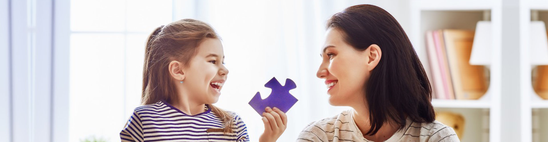 girl smiling and holding a puzzle piece while looking at her mom